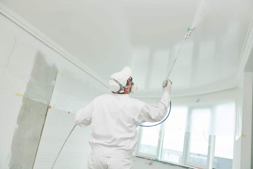 A commercial painter sprays paint on a ceiling